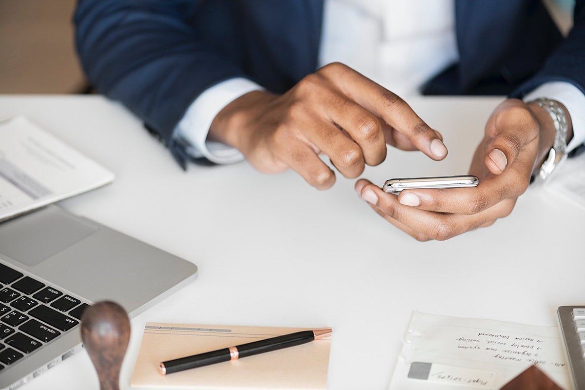 Businessman's hands using an Android phone, surrounded by laptop, notes, etc.